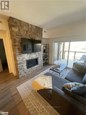Blue Mountains condo for rent - A living room with a stone fireplace and a flat screen TV mounted above it.