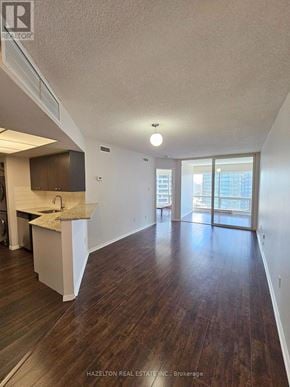 Toronto (Bay Street Corridor) condo for rent - A large, empty room with wood flooring and a kitchen area to the left.