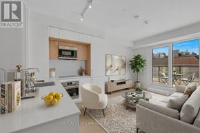 Toronto (Annex) condo for rent - A modern living room with a white sofa, a white chair, a coffee table, a bowl of lemons, a vase, a potted plant, a TV, a bookshelf, and a window.