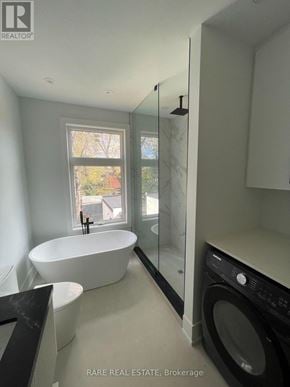 Toronto (Long Branch) apartment for rent - A modern bathroom with a large tub and a washer and dryer built into the cabinetry.