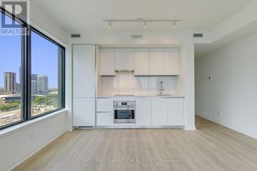 Mississauga (City Centre) condo for rent - A spacious kitchen with white cabinets and a large window overlooking the city.