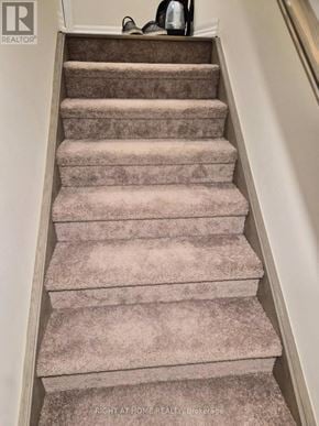 Clarington (Newcastle) apartment for rent - A beige carpeted staircase with a white wall on the left side.