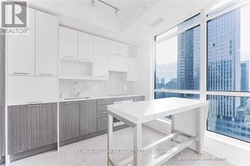 Toronto (Waterfront Communities) condo for rent - A white kitchen with a table and a window overlooking a city.