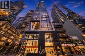 Toronto (Waterfront Communities) condo for rent - A tall building with a glass facade stands in front of other buildings at dusk.