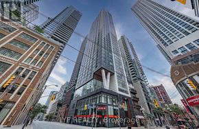 Toronto (Waterfront Communities) condo for rent - A tall building with a glass facade stands in the middle of a city street.