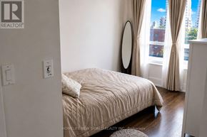 Toronto (North St. James Town) condo for rent - A bedroom with a bed, a round mirror, and a window with curtains.