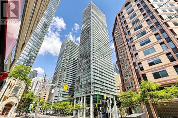 Toronto (Bay Street Corridor) condo for rent - A tall building with a glass facade stands in the middle of a city street.