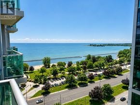 Toronto (South Parkdale) condo for rent - A view from a high-rise building overlooking a parking lot, trees, and a body of water.