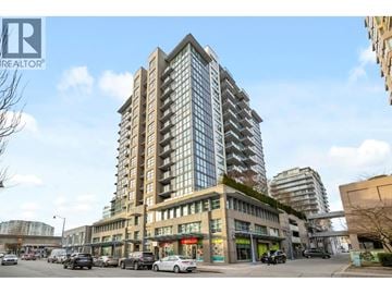Richmond apartment for rent - A tall building with a glass facade stands in the middle of a street with cars and other buildings in the background.