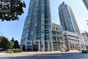Mississauga (City Centre) condo for rent - A tall building with many windows is in the background of a street scene.