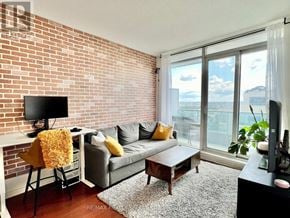 Mississauga (City Centre) condo for rent - A living room with a grey couch, a white desk, and a flat screen TV.