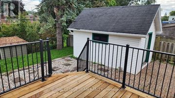 Ottawa apartment for rent - A small white building with a black roof and a green door is surrounded by a black metal fence.