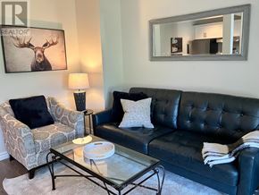 Blue Mountains townhouse for rent - A living room with a black couch, a glass coffee table, and a moose picture on the wall.
