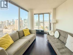 Vancouver apartment for rent - A living room with a grey couch and a city view through the window.