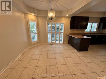 Brampton (Snelgrove) apartment for rent - A spacious room with tiled flooring and a kitchen area with dark brown cabinets.