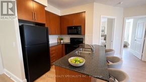 Mississauga (City Centre) condo for rent - A kitchen with a black fridge and microwave, a bowl of fruit on the island, and a sign that says RE/MAX REALTY SPECIALISTS INC. Brokerage.