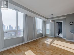 Mississauga (City Centre) condo for rent - A spacious room with wooden flooring and large windows overlooking a city skyline.