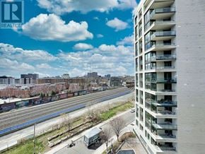 Toronto (Little Portugal) condo for rent - A tall white building with balconies is in the foreground with a train track and train in the background.