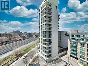 Toronto (Little Portugal) condo for rent - A tall white building with balconies is in the foreground with a train track and other buildings in the background.