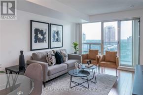Toronto (Willowdale East) condo for rent - A living room with a grey couch, two chairs, a coffee table, and a large window overlooking a cityscape.