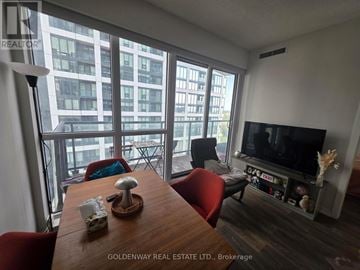 Toronto (Niagara) condo for rent - A living room with a wooden table and chairs, a flat screen TV, and a large window with a view of a city.