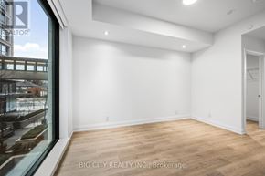Toronto (Thorncliffe Park) condo for rent - A spacious room with wooden flooring and white walls, with a view of a cityscape through a large window.