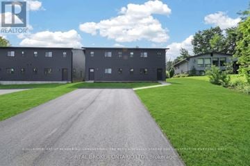 Tay (Port Mcnicoll) duplex for rent - A modern building with a grey facade is surrounded by a well-kept lawn and a clear sky.
