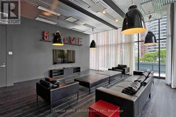 Toronto (Bay Street Corridor) condo for rent - A modern living room with a long black couch and a red ottoman.
