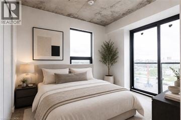 Brantford condo for rent - A bedroom with a large bed, a nightstand with a lamp, and a framed picture on the wall.