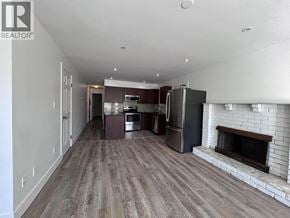 Vancouver apartment for rent - A large, empty living room with a fireplace and a kitchen area in the background.