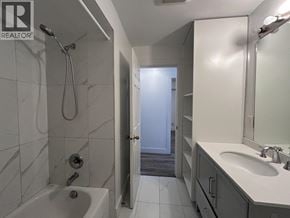 Vancouver apartment for rent - A bathroom with a white tub and sink, a shower with a hose, and a door leading to another room.