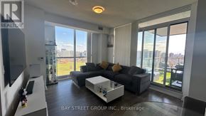 Toronto (Henry Farm) condo for rent - A living room with a grey sofa and a coffee table in front of a large window.