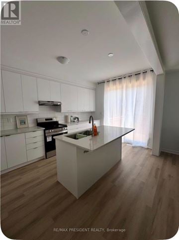 Barrie townhouse for rent - A modern kitchen with white cabinets and a wooden floor.