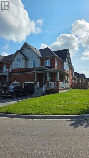 Clarington (Bowmanville) townhouse for rent - A large house with a red brick exterior and white trim is surrounded by a grassy lawn and a paved driveway.