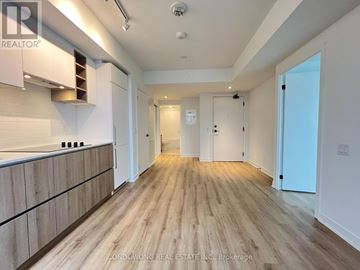 Toronto (Moss Park) condo for rent - A spacious room with wooden flooring and white walls, featuring a kitchen area with white cabinets and a countertop.