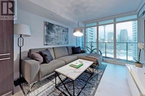 Toronto (Waterfront Communities) condo for rent - A living room with a grey couch, a coffee table, and a large window overlooking the city.