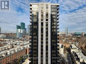 Toronto (Willowdale East) condo for rent - A tall building with a glass facade stands in the foreground of a cityscape.
