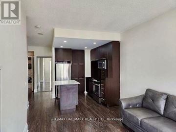 Toronto (Willowdale East) condo for rent - A modern kitchen with dark wood cabinets and a grey sofa in the foreground.