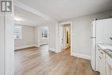Guelph (St. Patrick's Ward) triplex for rent - A spacious room with wooden flooring and white walls, featuring a kitchen area with white cabinets and a refrigerator.