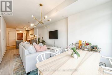 Toronto (Wychwood) condo for rent - A well-lit living room with a white sofa and a wooden dining table.