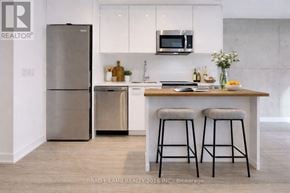 Toronto (Moss Park) condo for rent - A modern kitchen with a refrigerator, microwave, and bar stools.