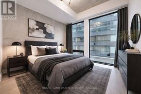 Toronto (Moss Park) condo for rent - A bedroom with a large bed, a nightstand, and a large window with a view of a building outside.