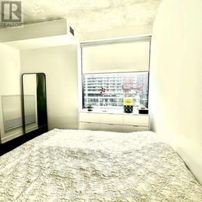 Toronto (Waterfront Communities) condo for rent - A bedroom with a large bed and a window overlooking a cityscape.