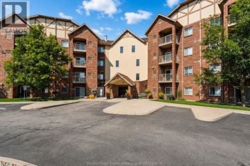Windsor condo for rent - A large apartment complex with a parking lot in front.