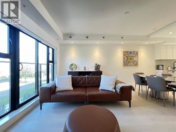 Vancouver townhouse for rent - A brown leather sofa with white pillows sits in a modern living room with a dining table and chairs.