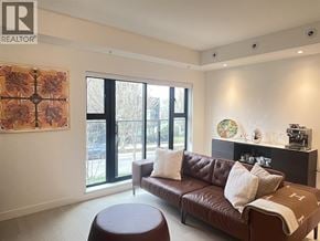 Vancouver townhouse for rent - A brown leather couch with a round ottoman in front of a window with a painting hanging on the wall.