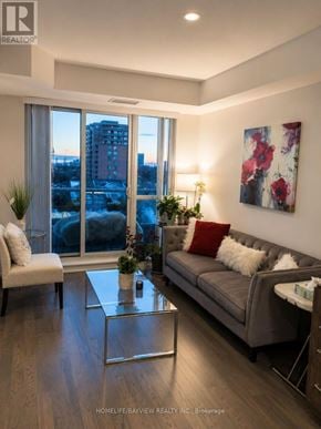 Richmond Hill (Langstaff) condo for rent - A living room with a grey couch, a coffee table, and a large window with a view of the city.