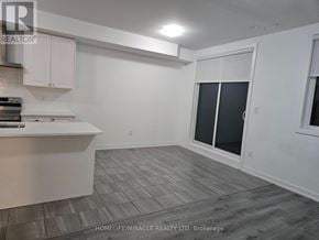 Barrie (Innis-Shore) townhouse for rent - A spacious room with a kitchen area and a sliding glass door.
