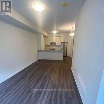 Vaughan (Vaughan Corporate Centre) townhouse for rent - A room with wooden flooring and white walls, with a kitchen area visible in the background.