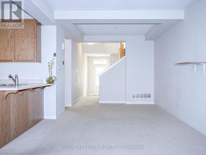 Ottawa townhouse for rent - A spacious, empty room with a kitchen area to the left and a staircase in the distance.